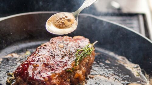En närbild på en kock som steker kött i en gjutjärnspanna