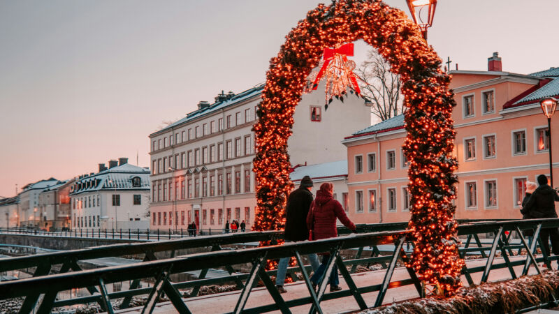 Ett par går över en bro dekorerad med med juliga, lysande girlanger