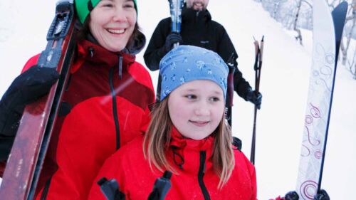 En mamma, pappa och ett barn bär på skidor i ett vinterlandskap
