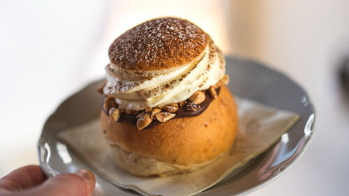 En hand håller en tallrik med en choklad-semla på