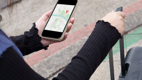 En kvinna håller i en resväska och en mobil med kartfunktionen uppe