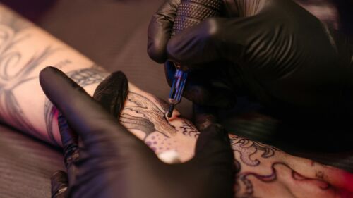 Närbild på en tatuerare som tatuerar en kvinnas arm